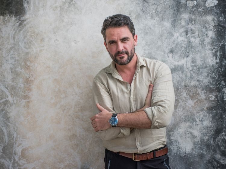 Explorer and author Levison Wood stands in a casual shirt and jeans against a grey background