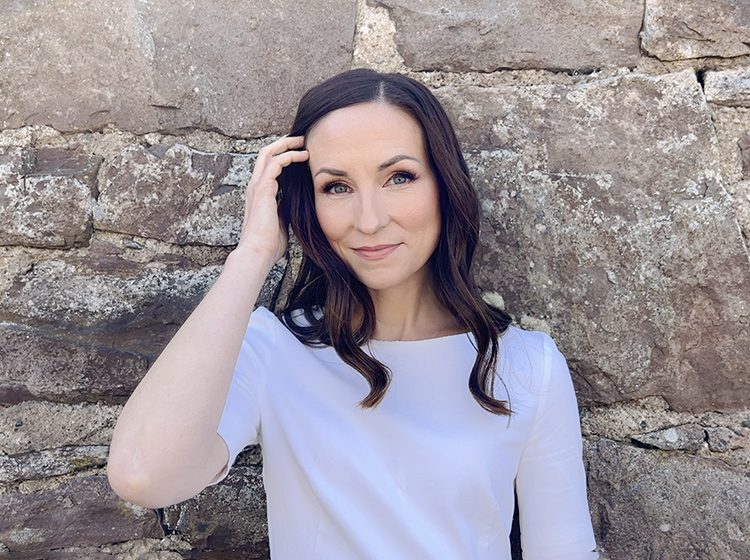 Julie Fowlis standing in front of a stone wall. Photo by Wild Soul Photography.