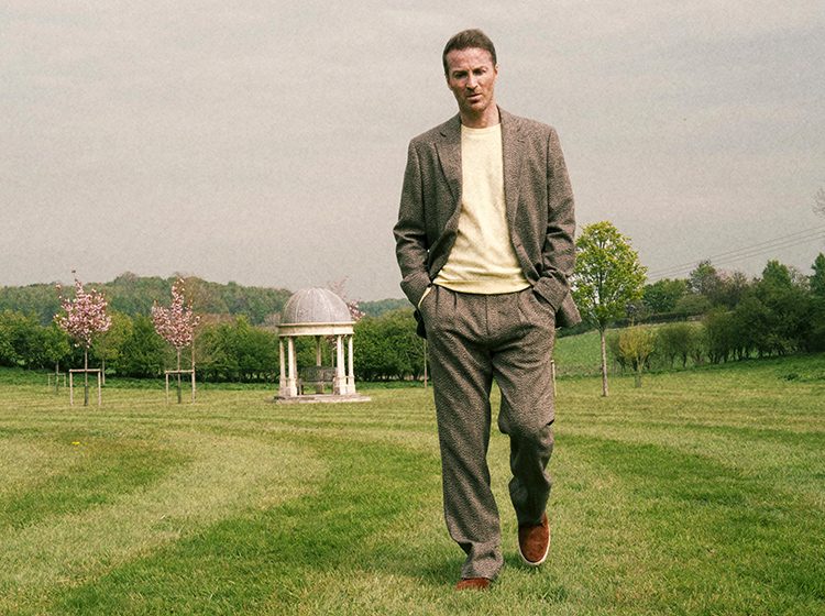 RIOPY walking across a mown field with pink-blossomed trees in the distance